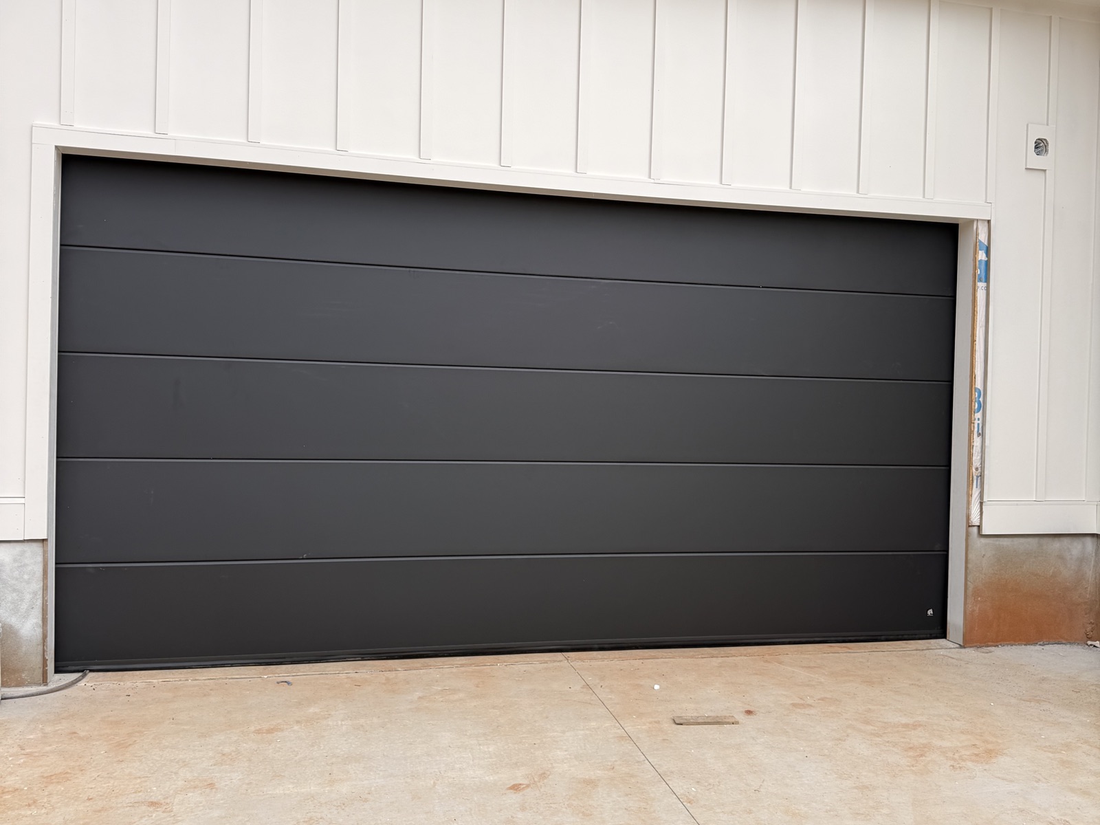 Matte black modern flush garage door on a white board-and-batten farmhouse in Boiling Springs SC