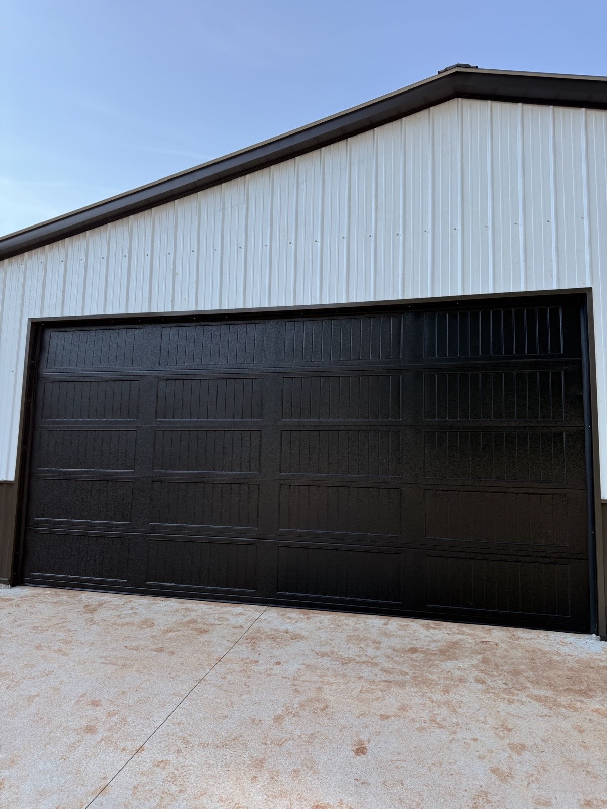 Black long-panel steel garage door installed on a white metal barn shop