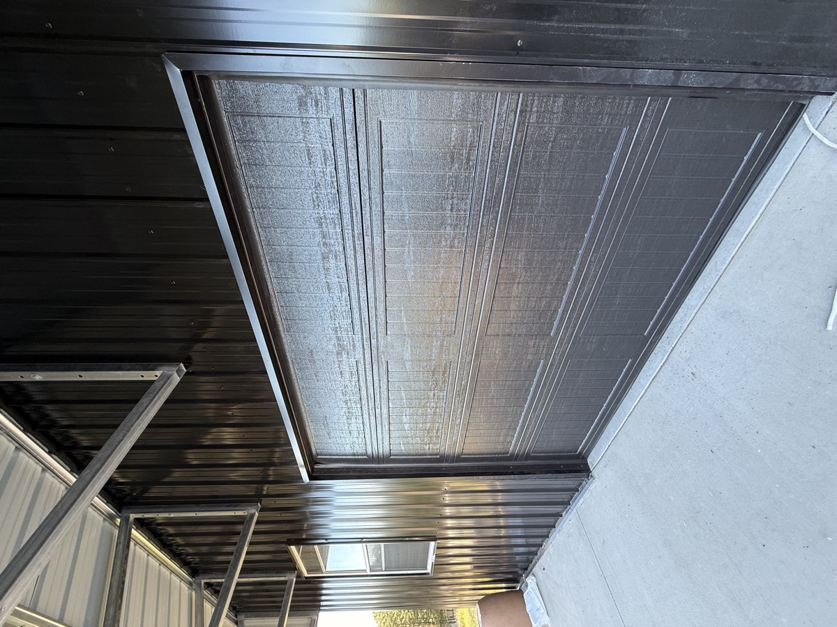 Dark woodgrain-finish garage door on a black metal building near Spartanburg SC