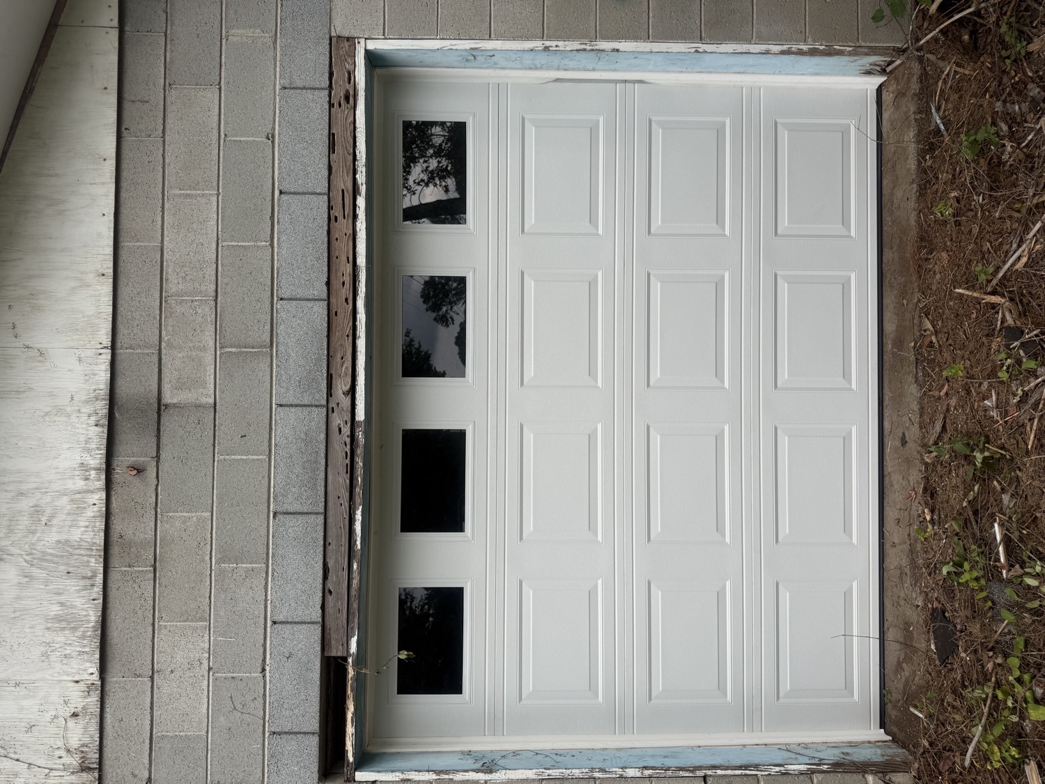 After: a new white raised-panel garage door with windows installed in the same cinder-block garage
