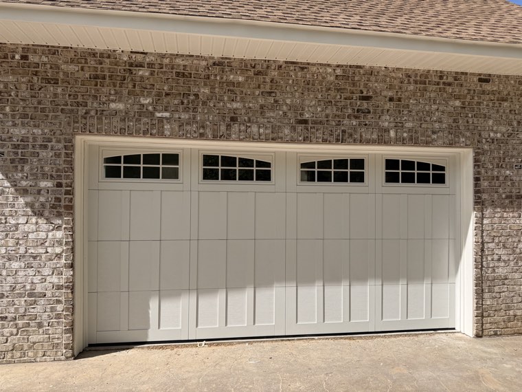 Close view of an almond carriage-style double garage door with arched windows on a brick home