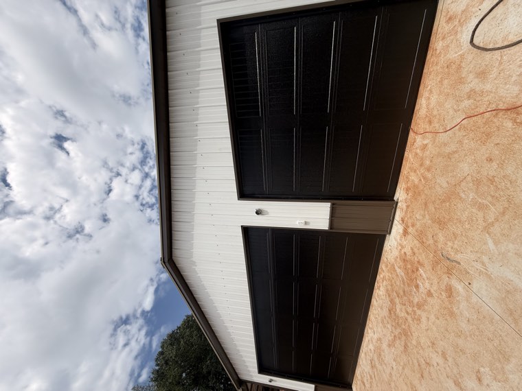 Two black garage doors installed on a white pole barn with brown wainscot