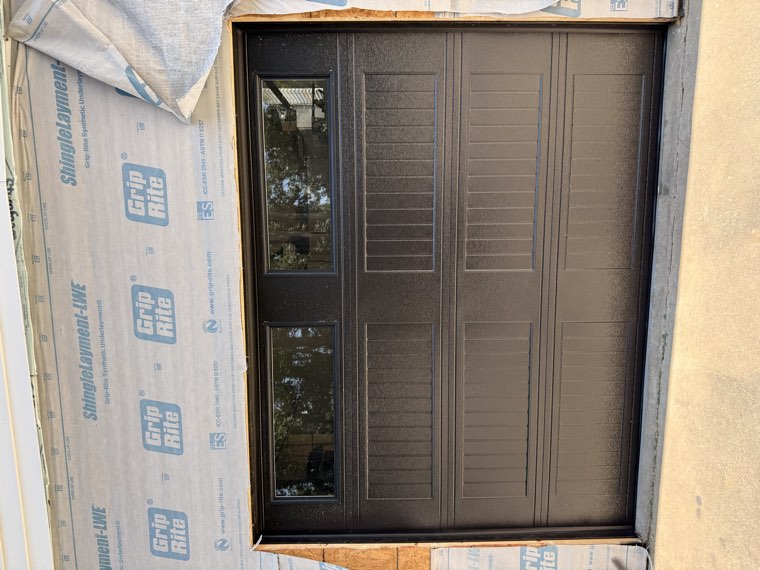 Bronze long-panel garage door with window sections installed on a home still under construction