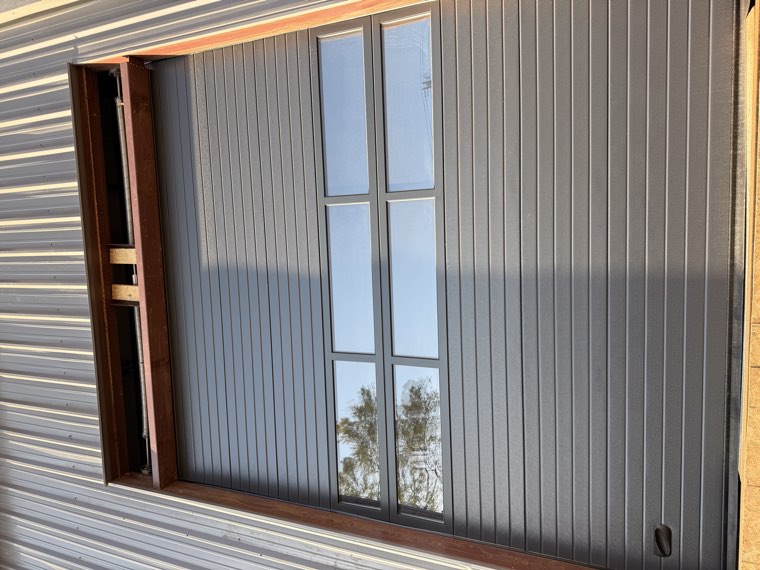 Tall charcoal commercial overhead door with window sections on a metal shop building, angled view
