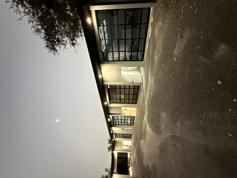 Row of black full-view glass garage doors lit up at night on a commercial shop