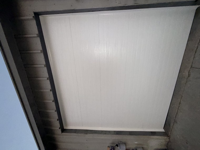 White insulated commercial garage door installed on a metal building at dusk