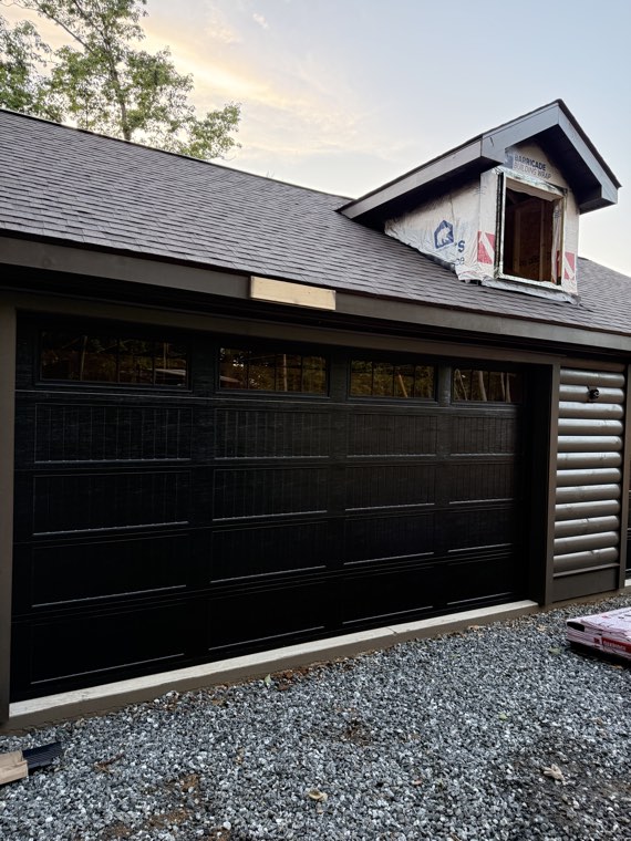 Dark brown carriage-style double garage door with a row of windows on a new detached garage