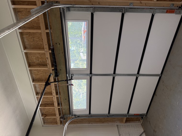 Interior of a new garage showing a white insulated door with a window row and torsion spring