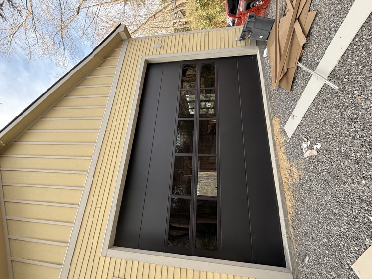 Black modern garage door with a full row of tinted windows on a yellow-sided home in the Upstate of South Carolina