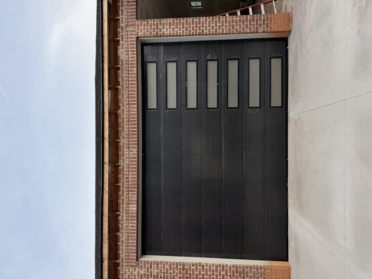 Black modern garage door with a vertical column of frosted windows installed on a brick home in Greenville, SC