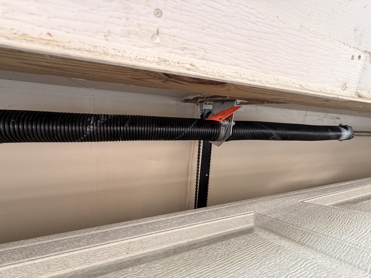 Close-up of a garage door torsion spring, lift cable and drum at the side of the opening