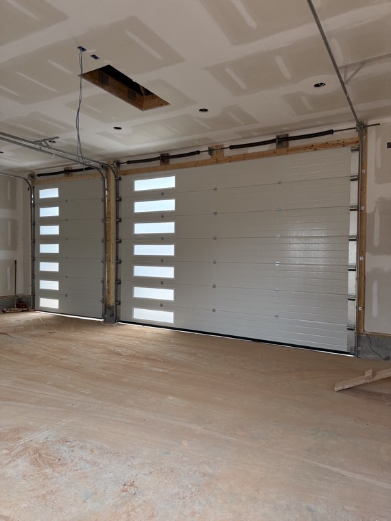Two white garage doors with vertical window columns seen from inside a new two-car garage