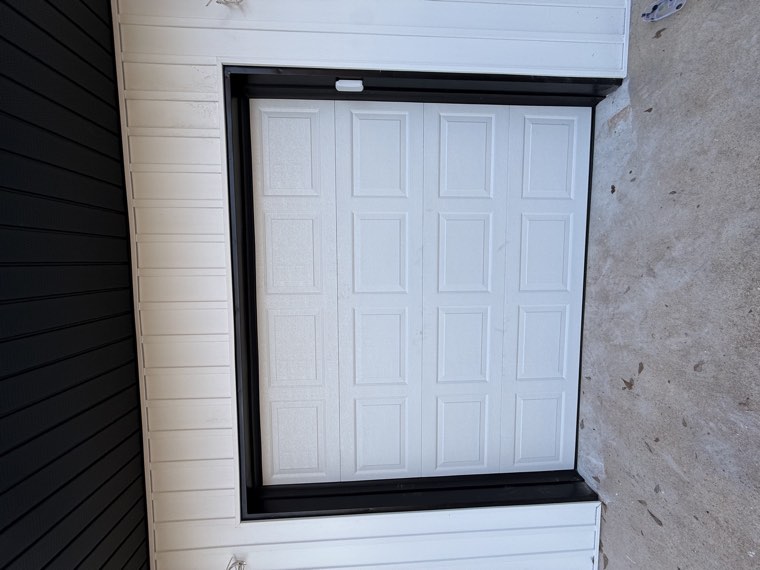 White short raised-panel single garage door installed on a white metal building with black trim